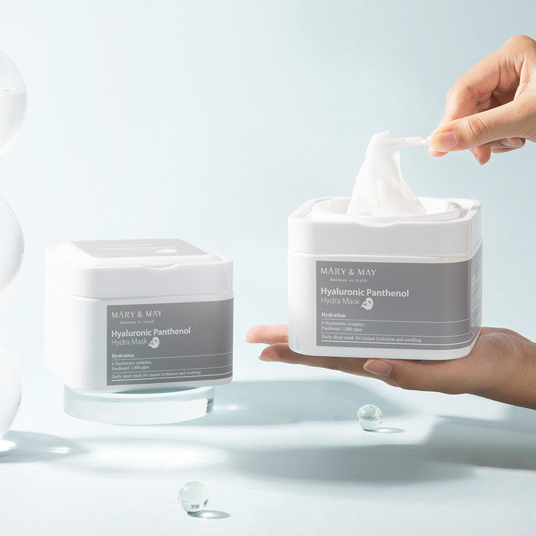 Person using MARY & MAY Hyaluronic Panthenol Hydra Mask x30 with product containers in the background