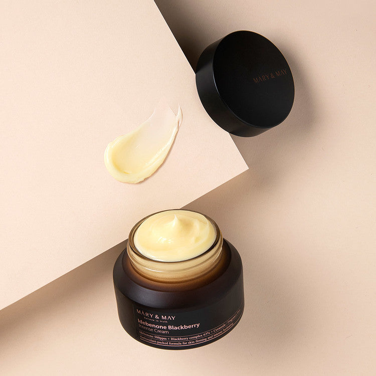 Open jar of MARY & MAY Idebenone Blackberry Intense Cream 70g with cream swatch on beige background.