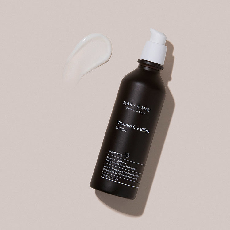 Bottle of MARY & MAY Vitamin C + Bifida Lotion 120ml with lotion smear on beige background