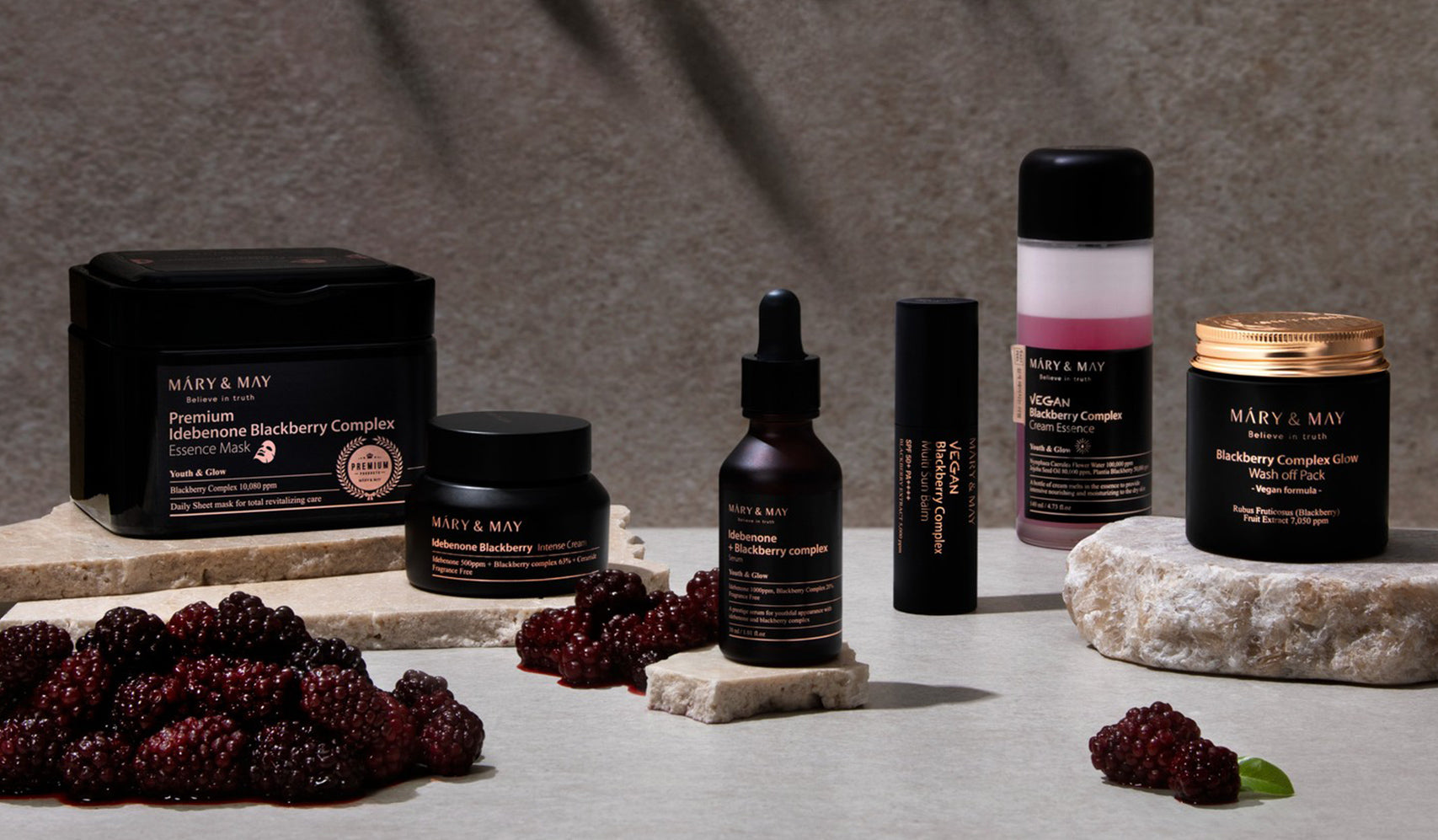 Skin care products with blackberries, featuring Mary & May's BlackBerry Complex Essence collection, displayed on a stone surface.
