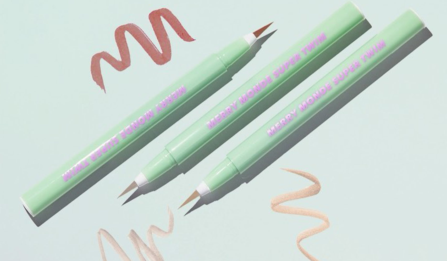 Three green dual-tip brush pens with pink and beige strokes on a light blue background.