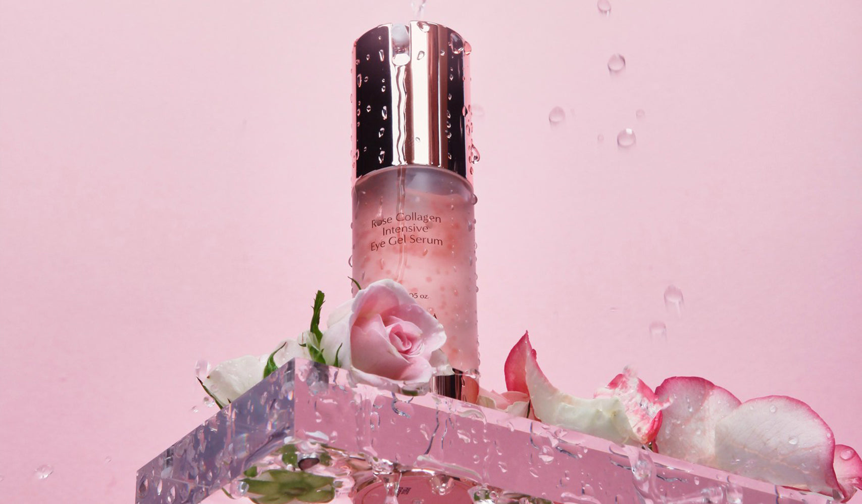 Luxury skincare serum bottle with rose petals and water droplets on a pink background