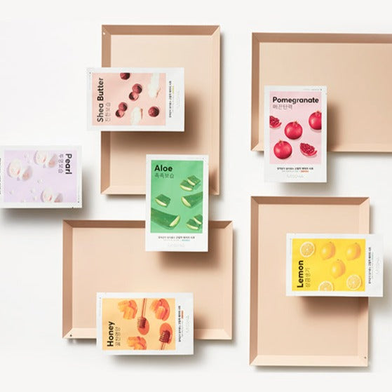 Assorted MISSHA Airy Fit Sheet Mask packs displayed on beige trays including flavors like Aloe, Lemon, Honey, and Pomegranate.