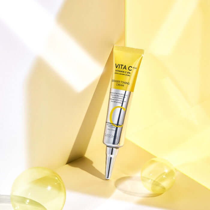MISSHA Vita C Plus Eraser Toning Cream 30ml in vibrant yellow packaging, placed elegantly on a reflective surface.