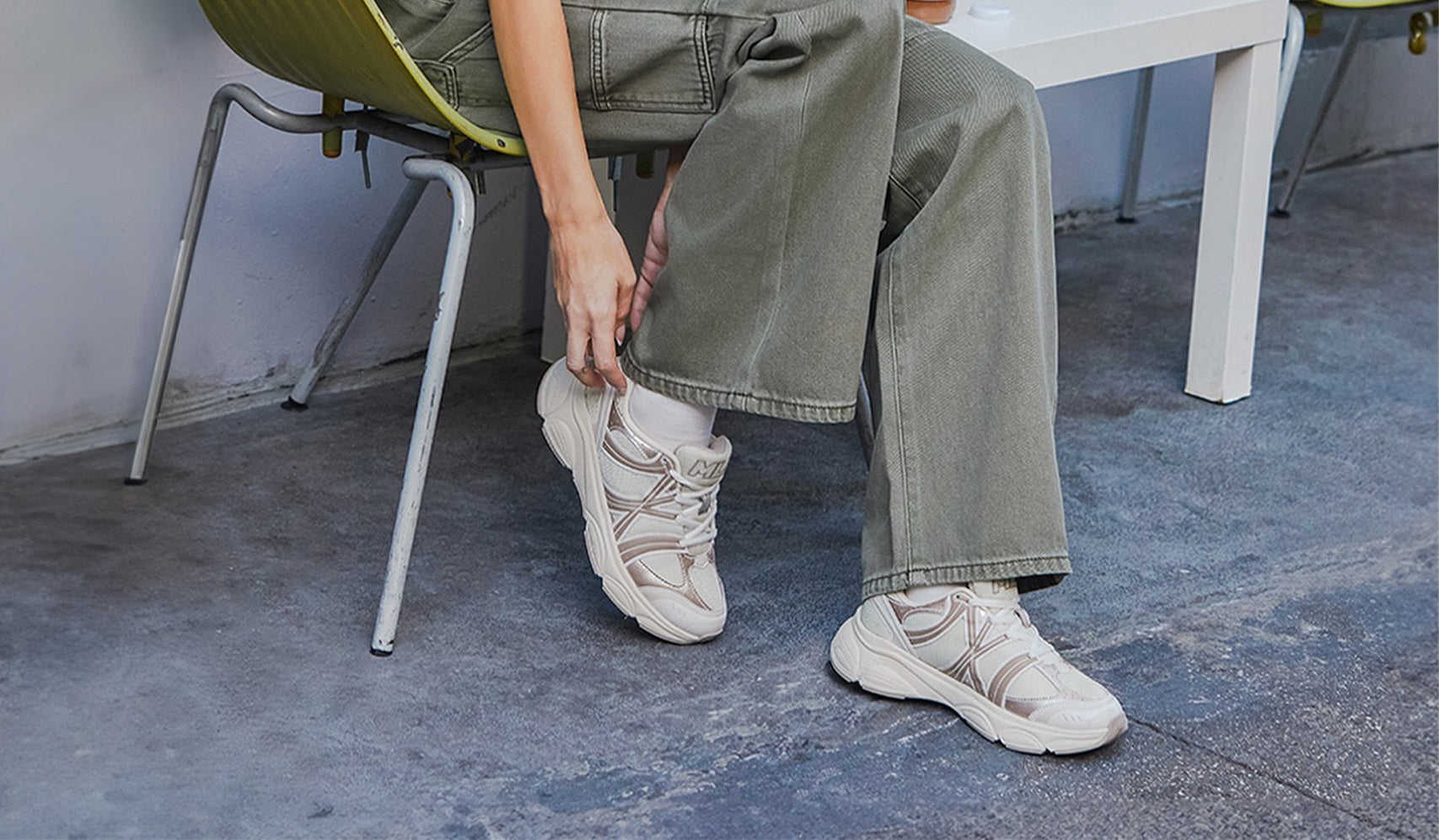 Person wearing beige sneakers and green pants sitting on a chair outdoors.