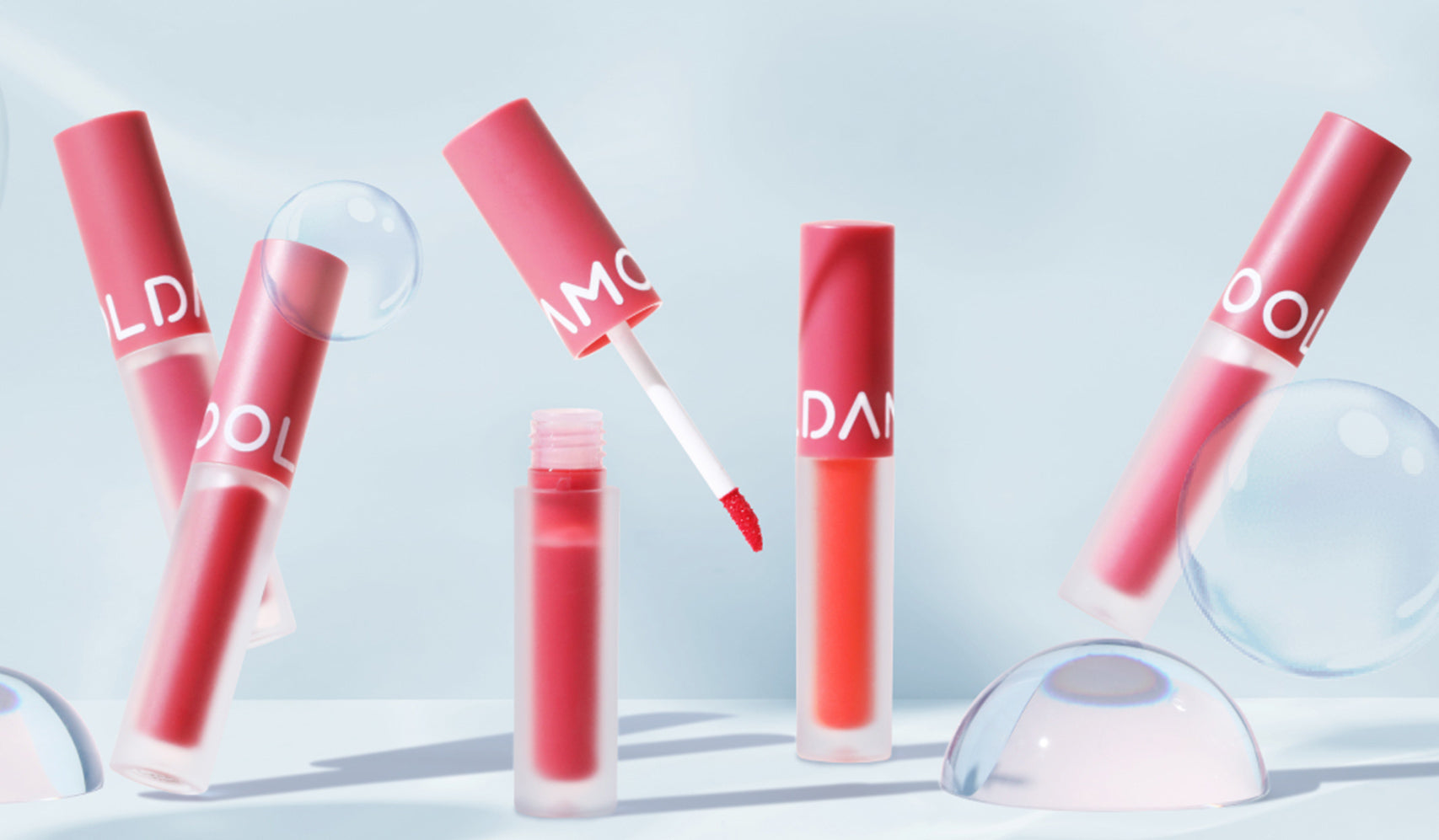 Collection of red lip glosses on a light background with bubbles, showcasing beauty and elegance.