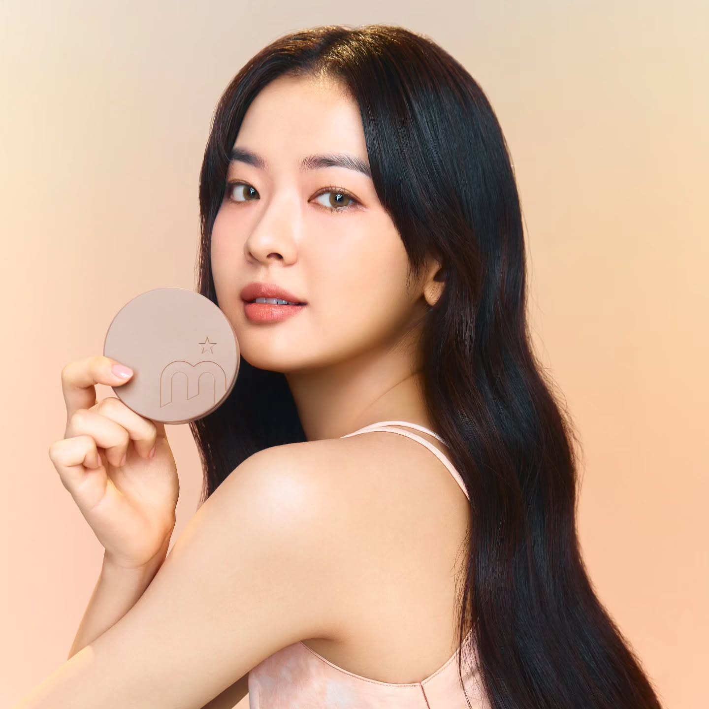 Woman holding MOONSHOT Conscious Fit Cushion Foundation with soft focus background.