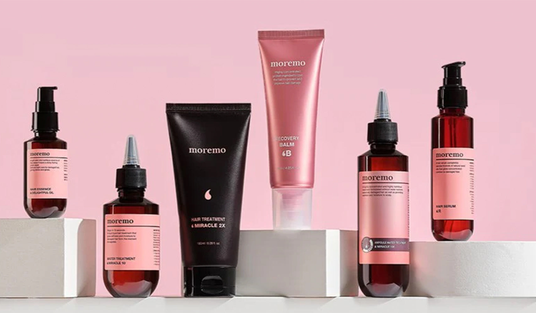 Skincare products arranged on white blocks against a pink background, featuring various bottles and tubes of beauty treatments.