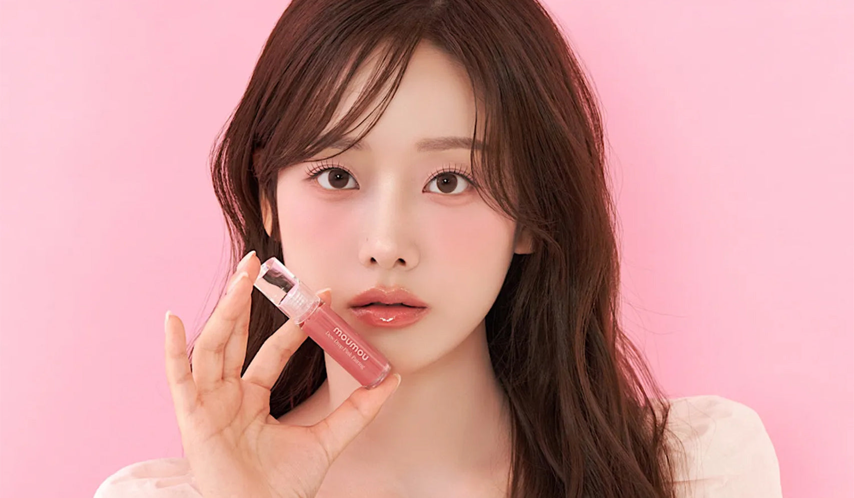 Person holding a pink lip gloss against a pink background