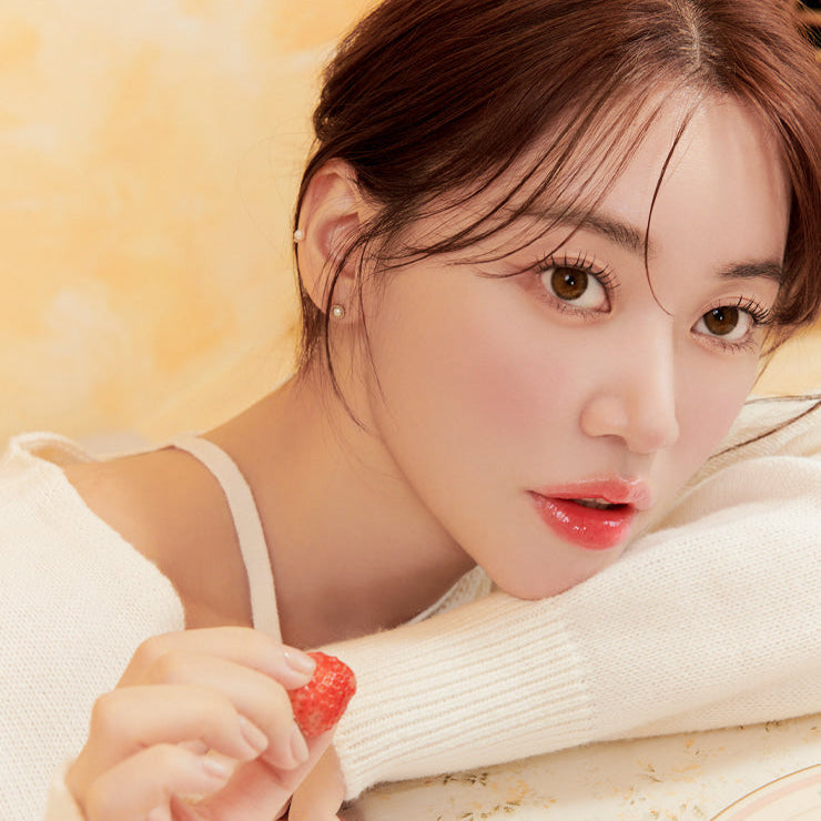 Woman holding a strawberry, showcasing natural beauty with soft lighting and a serene expression.