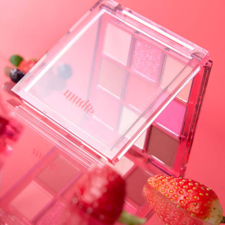 MUDE Feel Lively Eyeshadow Palette with vibrant colors, surrounded by fresh strawberries and berries, on a reflective surface.