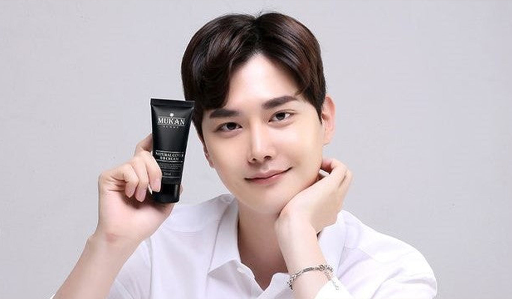 Person holding skincare product tube, smiling