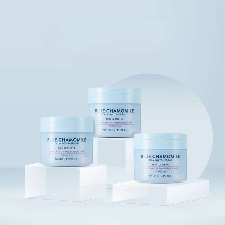Three jars of NATURE REPUBLIC Blue Chamomile Calming Toner Pads 120g displayed elegantly on white blocks against a blue background.