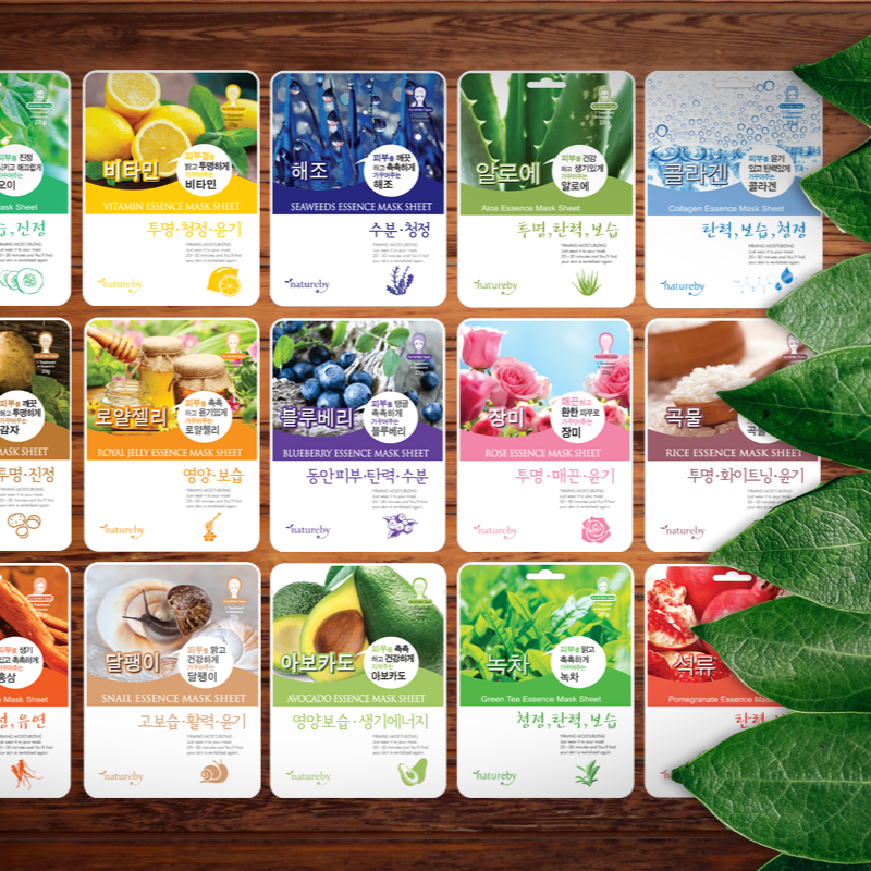 NATUREBY Essence Mask Pack 1+1 variety on wooden table with green leaves, including vitamin, seaweed, avocado, and more skincare masks