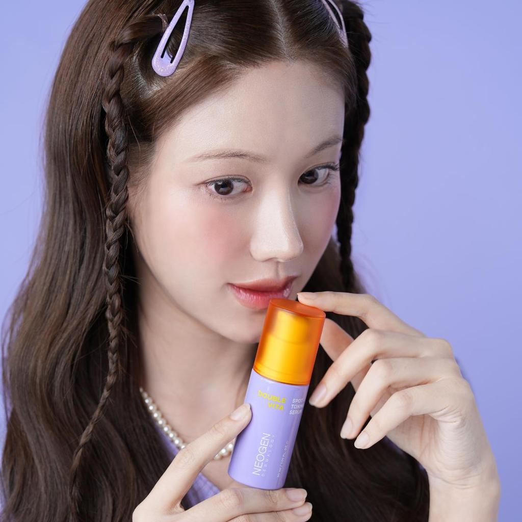 Model holding NEOGEN Double Vita Spot Toning Serum 30ml in purple packaging
