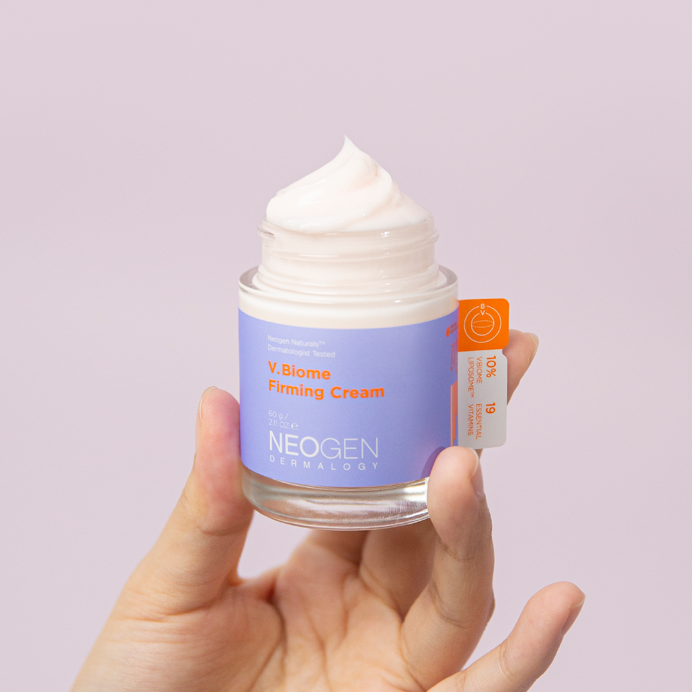 Person holding a jar of NEOGEN V Biome Firming Cream 60g with lid off, showcasing the product texture against a light background.