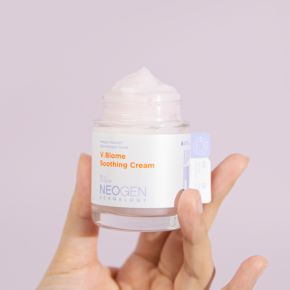 Hand holding NEOGEN V Biome Soothing Cream 60g jar with pink cream against a light background.