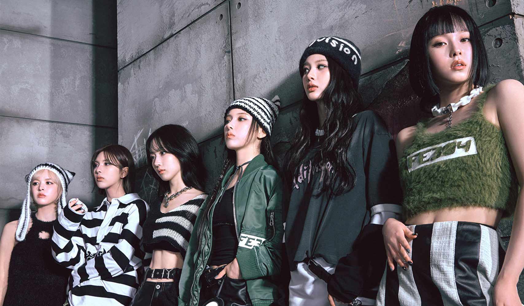 Group of six fashionable young women posing against a concrete wall, wearing trendy streetwear and knit accessories.