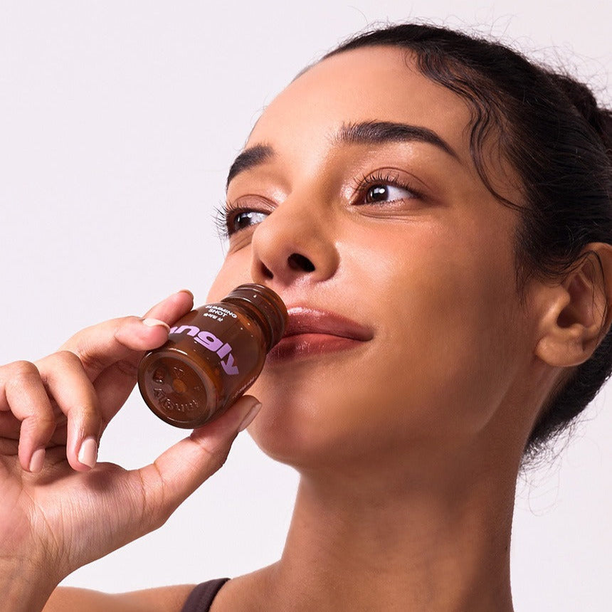 Woman enjoying a NOTHING BETTER Tangly Slimming Shot bottle, promoting wellness and slimming benefits.