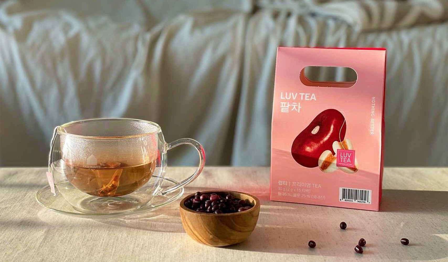 Glass cup of tea next to Luv Tea packaging and small bowl of beans on a table with soft lighting.