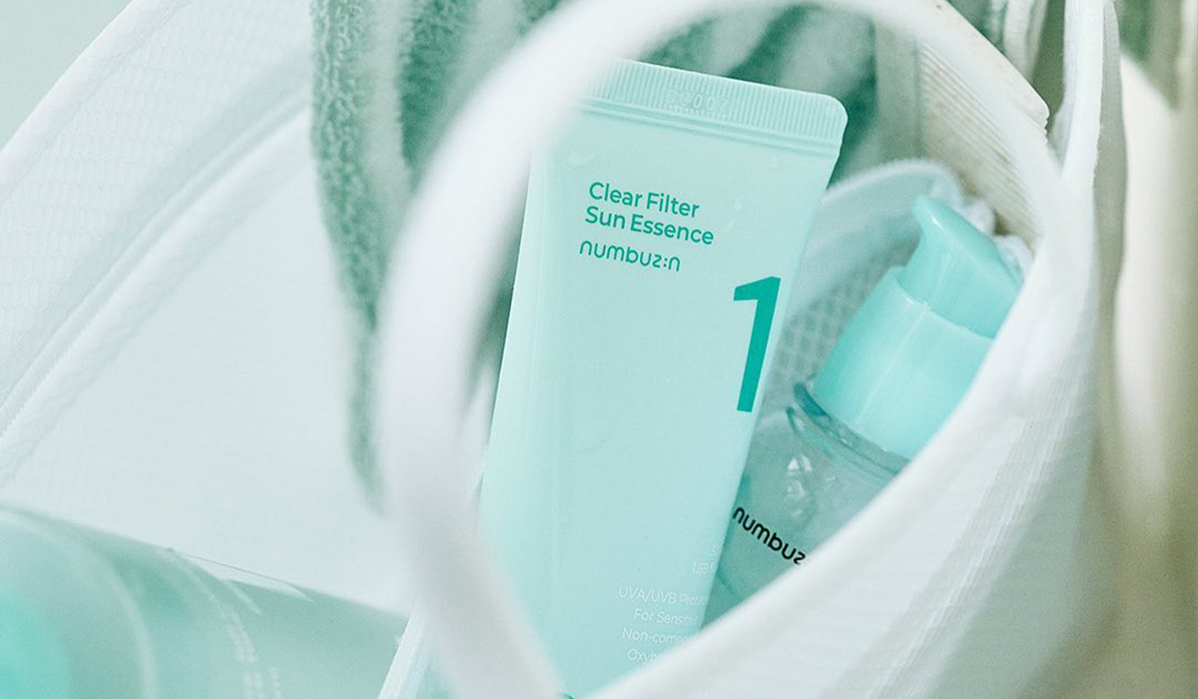 Skincare products in bag, including Clear Filter Sun Essence by Numbuzin, with soft lighting and green color scheme.