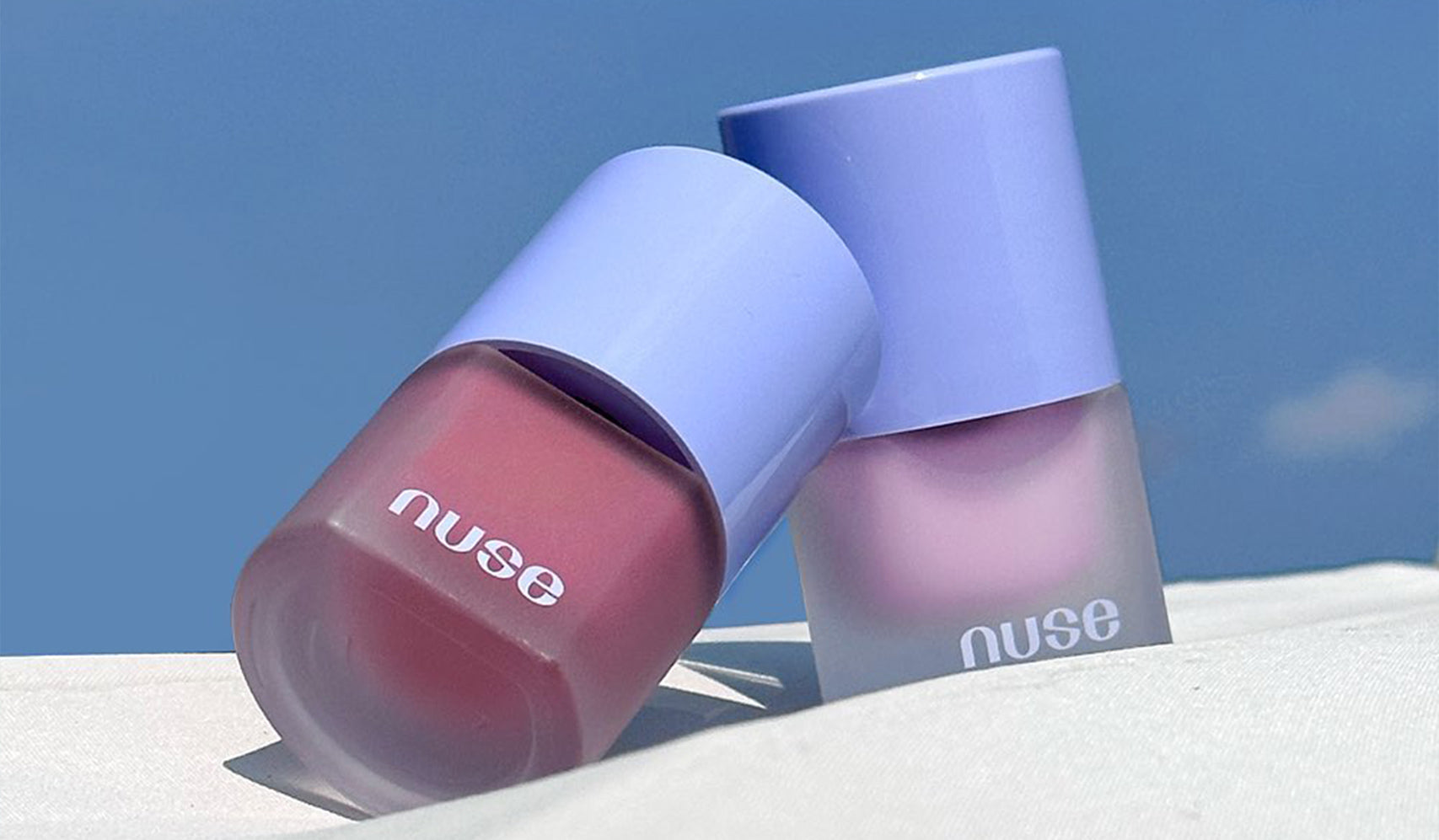 Nuse nail polish bottles in lavender and pink shades under a blue sky.