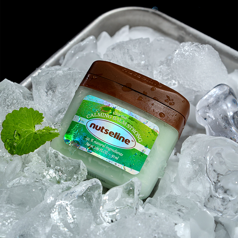 NUTSELINE Cica Nut Calming Balm Strong 50ml jar surrounded by ice and a green leaf, highlighting natural cooling ingredients.