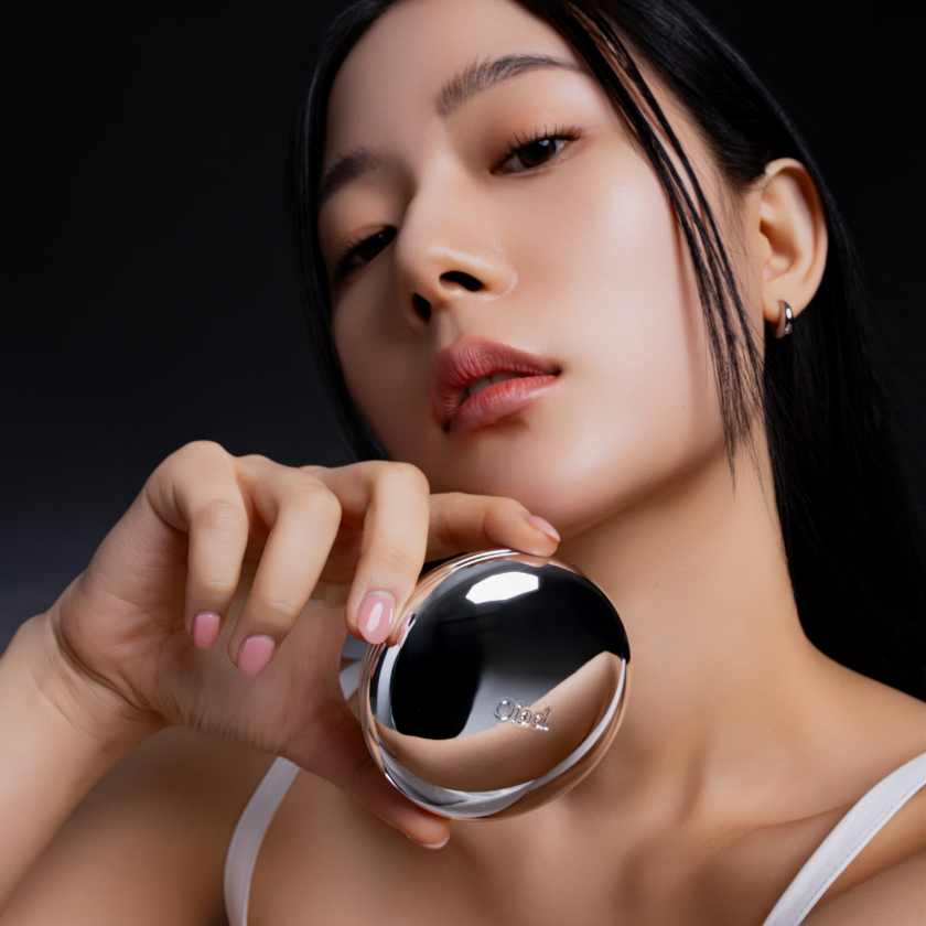 Woman holding OIAD Pore Perfecting Mirror Moon Cushion close to her face, showcasing skincare product's elegant design and functionality.