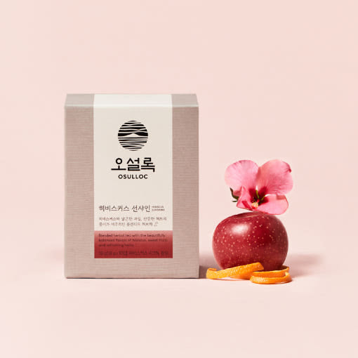 Box of OSULLOC Hbiscus Sunshine Tea 10p with apple, orange slices, and hibiscus flower on a pink background.