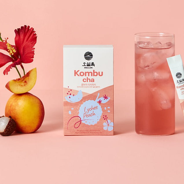 OSULLOC Kombucha Lychee Peach & Cala Mango Set featuring a box, fruit, and a glass of iced drink on a pink background.