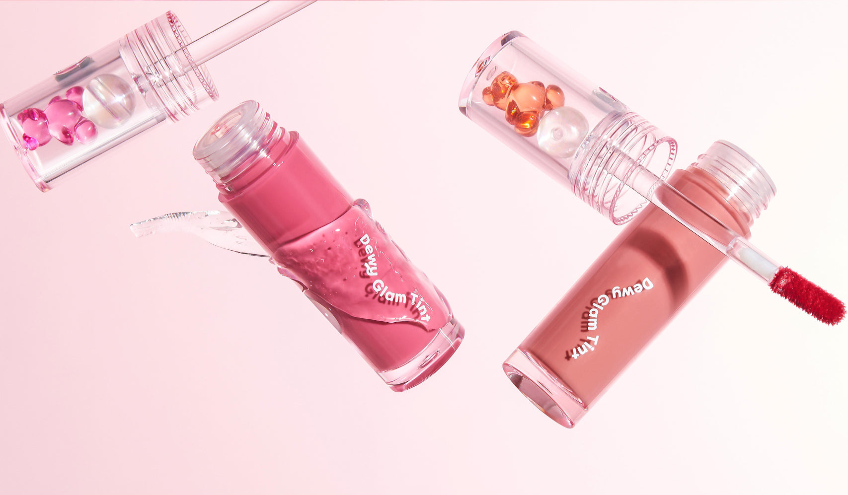 Assorted pink and nude lip gloss tubes with applicators and decorative beads on a pink background.