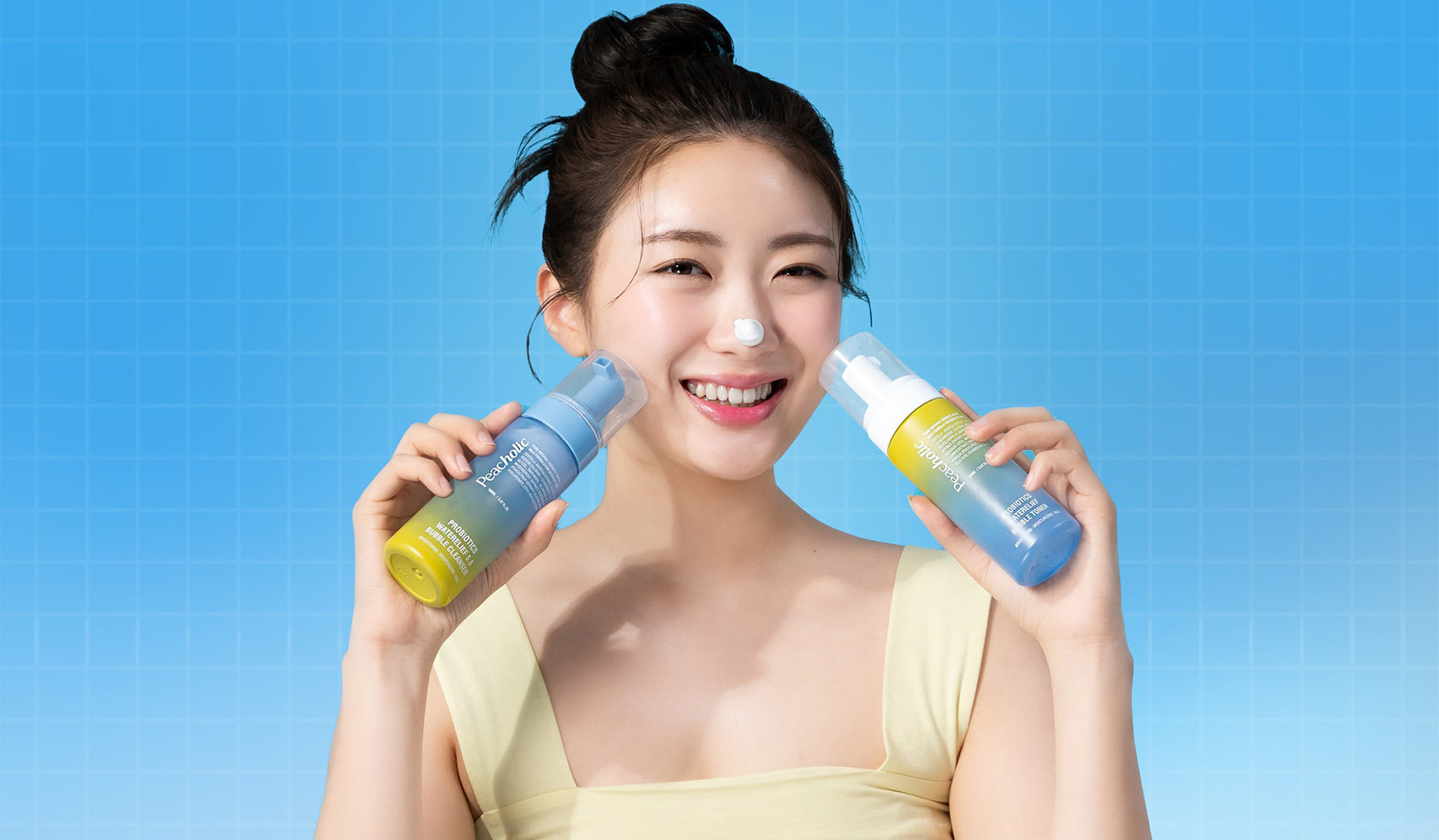 Young woman smiling while holding skincare bottles against a blue background