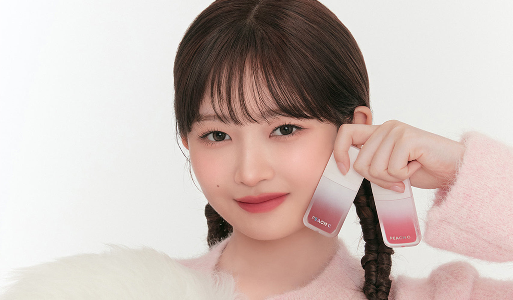 Smiling person holding two makeup products against a white background.