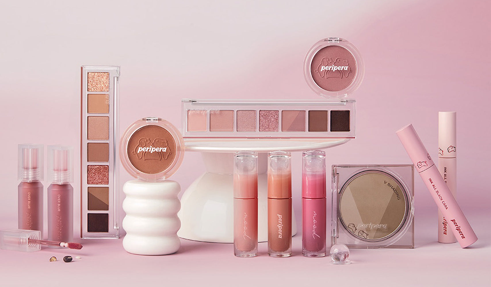 Collection of pink and nude Peripera makeup products including lip tints and eye shadow palettes, arranged on a pink background.