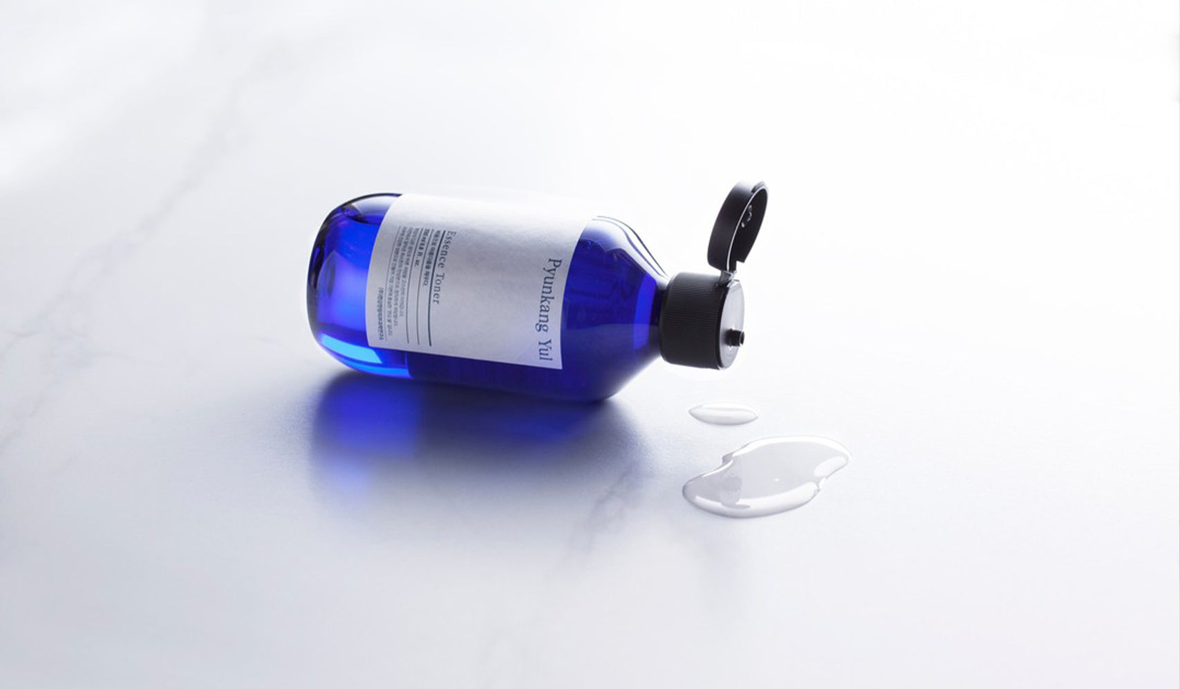 Open blue bottle with liquid spilled on white surface, close-up view.