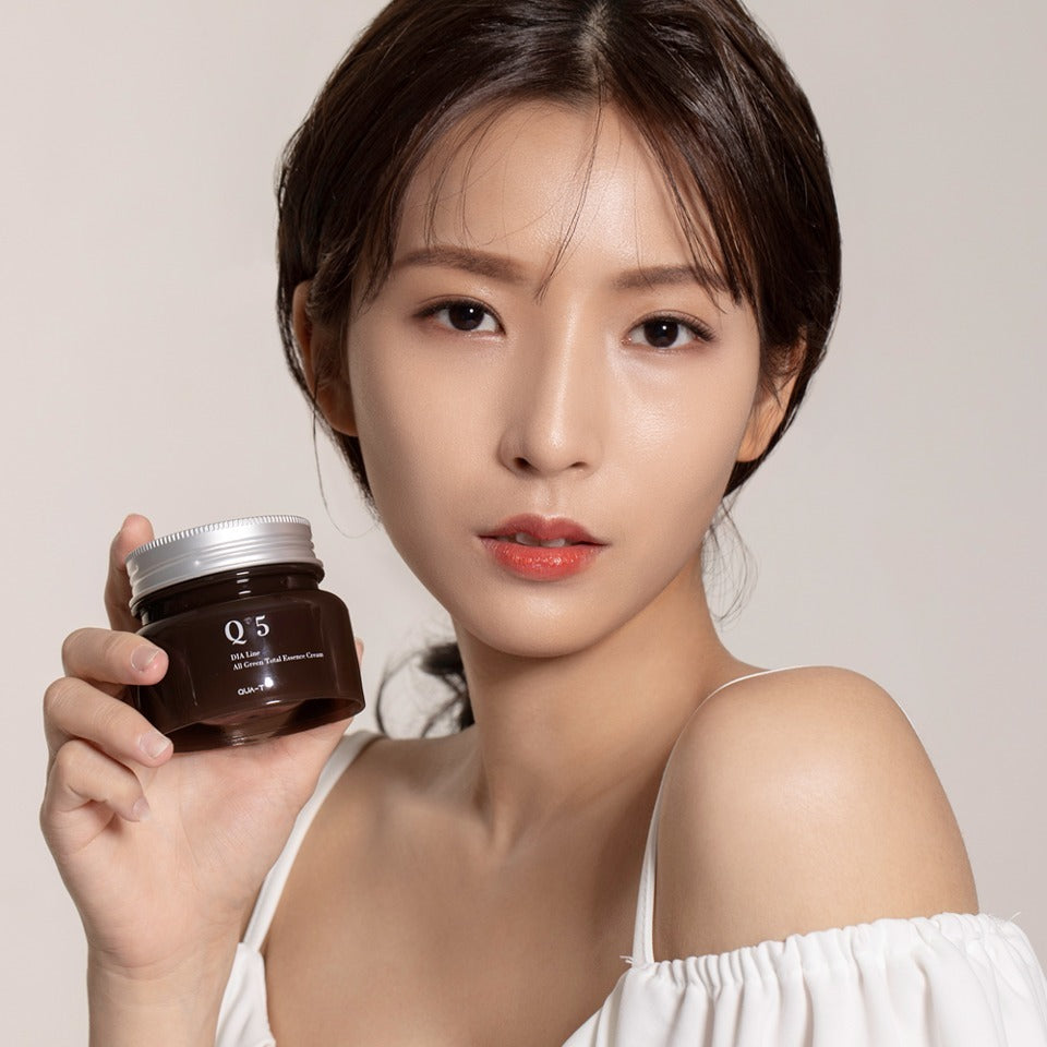 Person holding a jar of QUA-T Dia All Green Total Essence Cream 100ml, suitable for skincare routines.