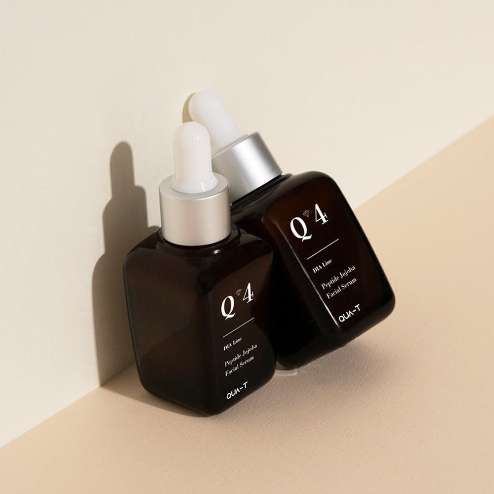 Two bottles of QUA-T Dia Peptide Jojoba Facial Serum 30ml on a beige surface