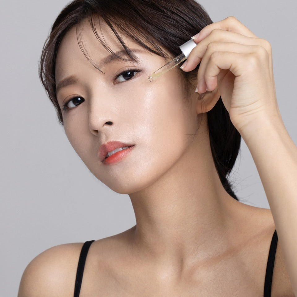 Woman applying QUA-T Dia Peptide Jojoba Facial Serum 30ml to her face for skincare.