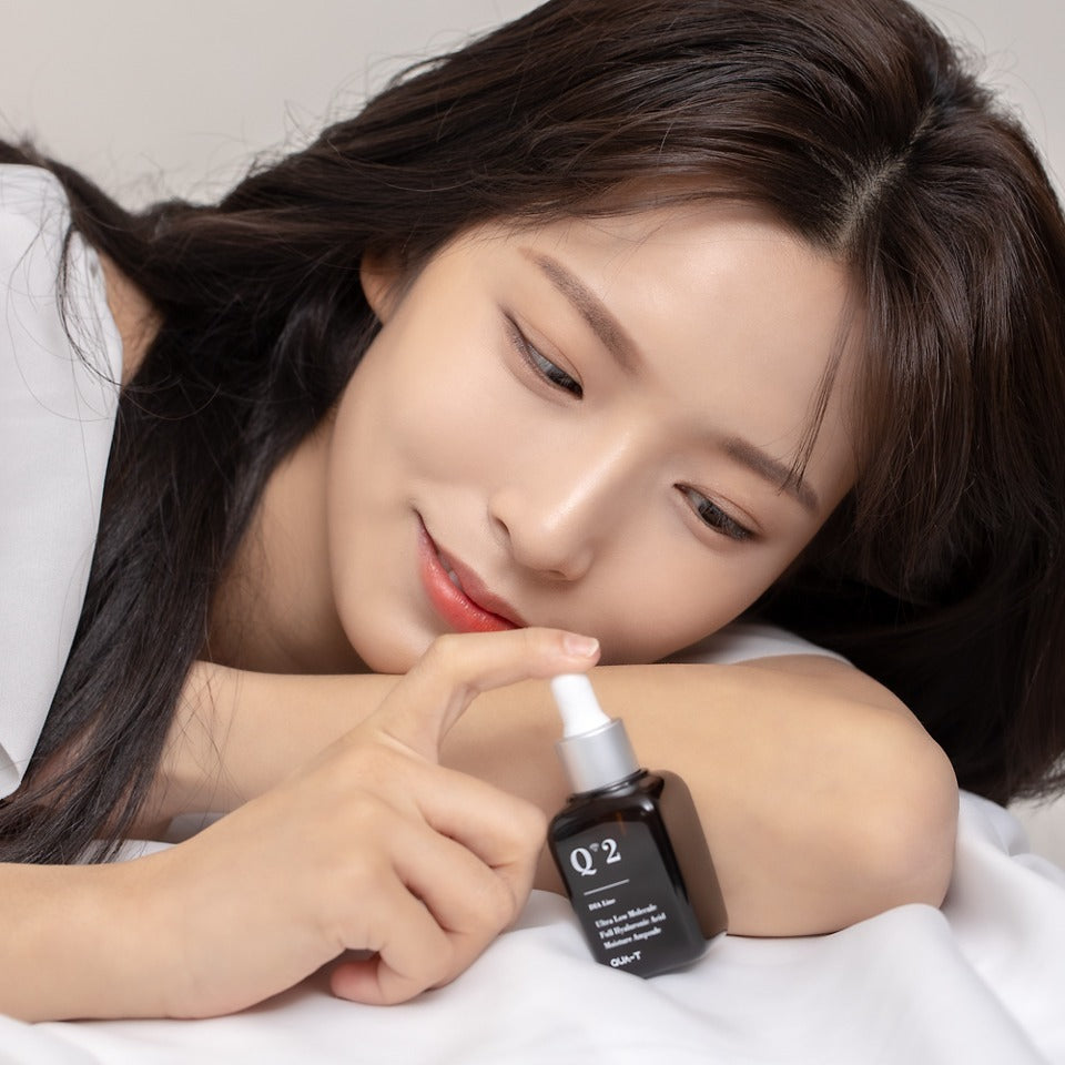 Woman holding QUA-T Dia ultra-low molecular weight full hyaluronic acid moisture ampoule 30ml product bottle.