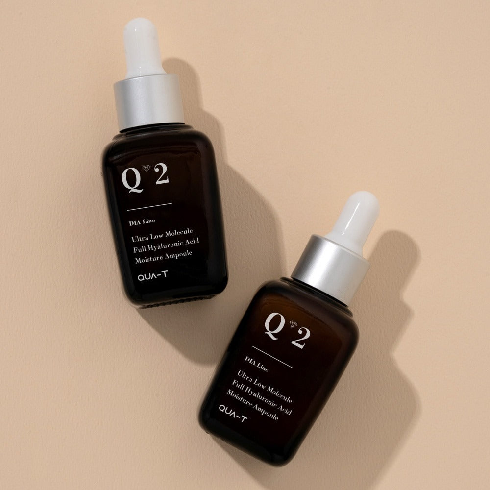 Two bottles of QUA-T Dia ultra-low molecular weight full hyaluronic acid moisture ampoule 30ml on a beige surface