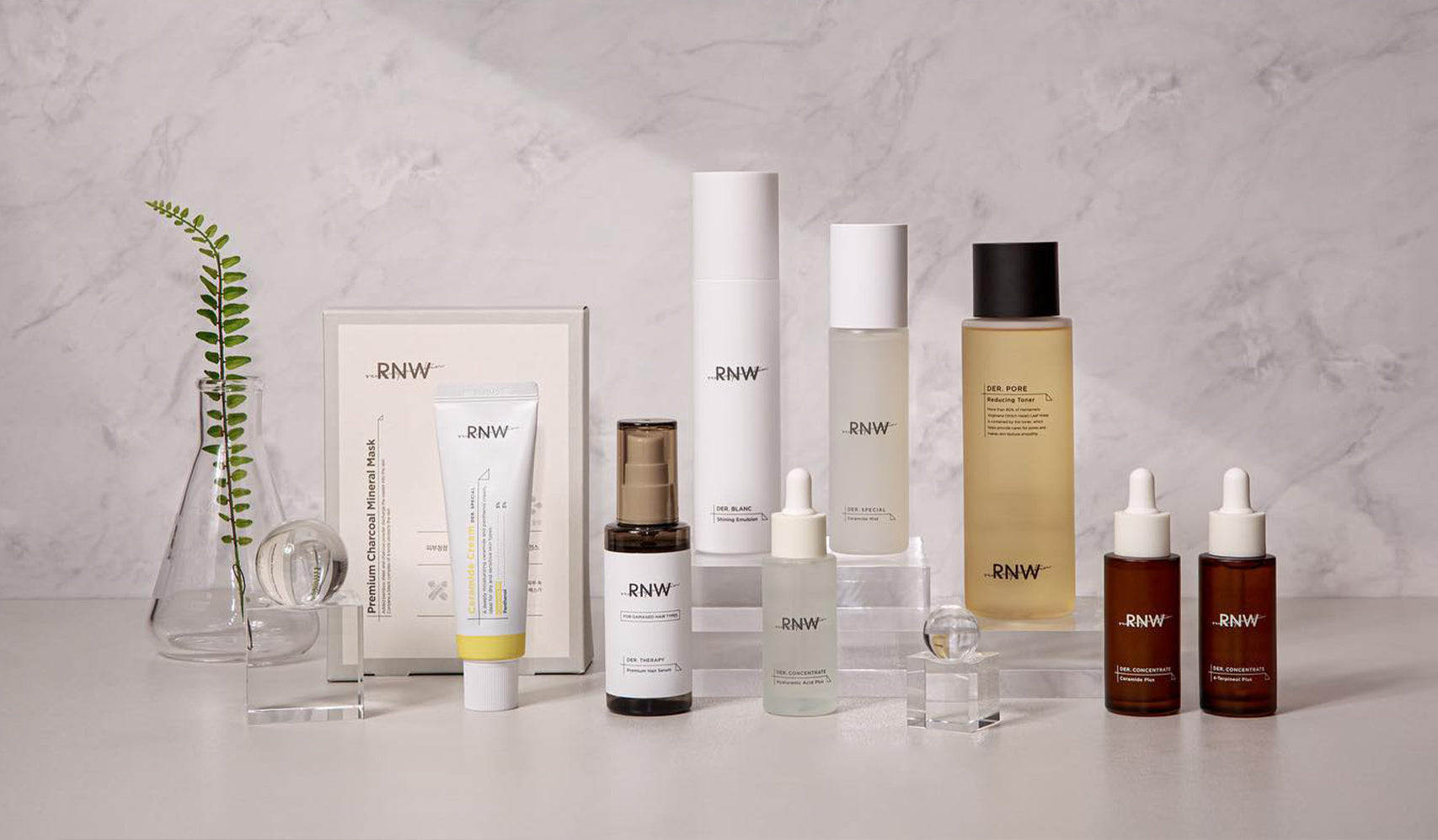 Collection of RNW skincare products arranged on a marble surface with decorative plant and glass elements.