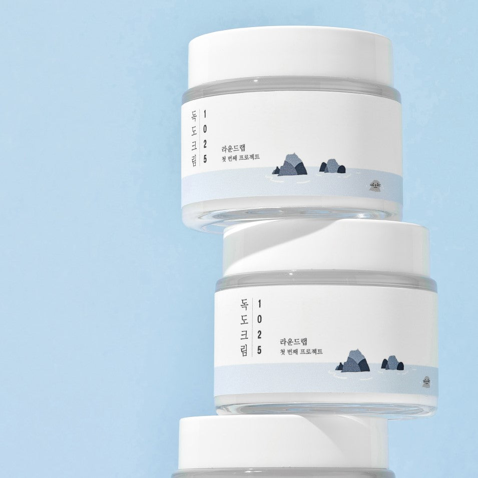 Image of ROUND LAB 1025 Dokdo Cream 80ml stacked jars with minimalist design on blue background