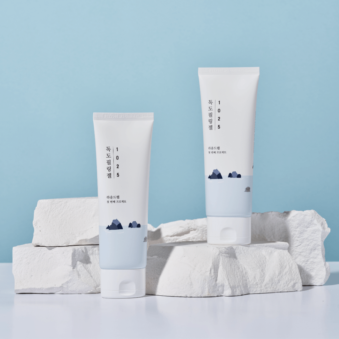 Two tubes of ROUND LAB 1025 Dokdo Peeling Gel 120ml placed on white rocks against a blue background for skincare routine.