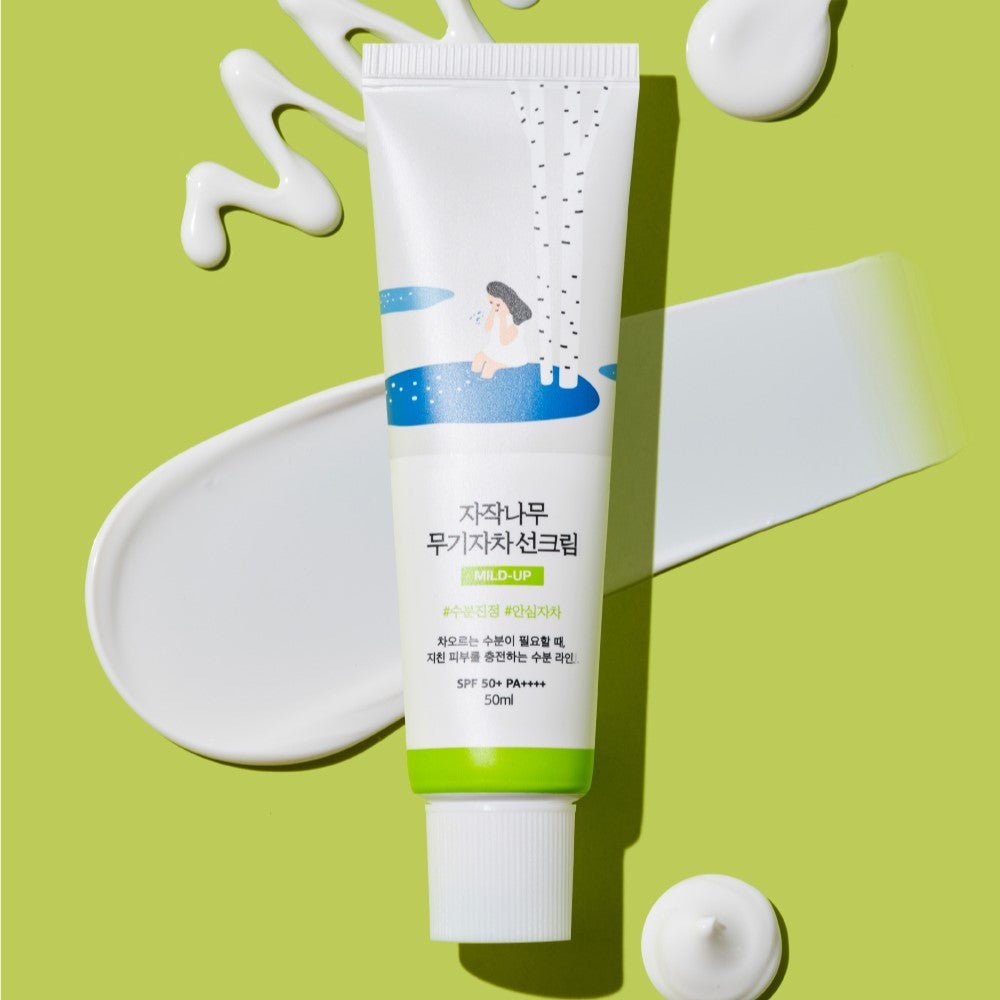 ROUND LAB Birch Juice Moisturizing Mild-Up Sunscreen 50ml on a green background with product swatches