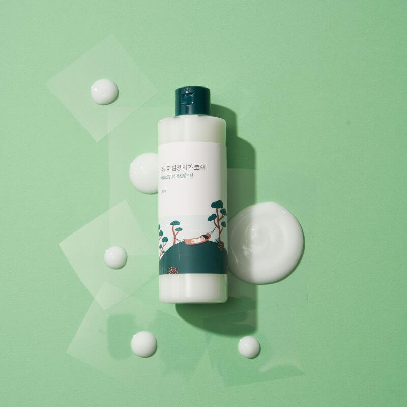 ROUND LAB Pine Calming Cica Lotion 250ml bottle on green background with lotion droplets.