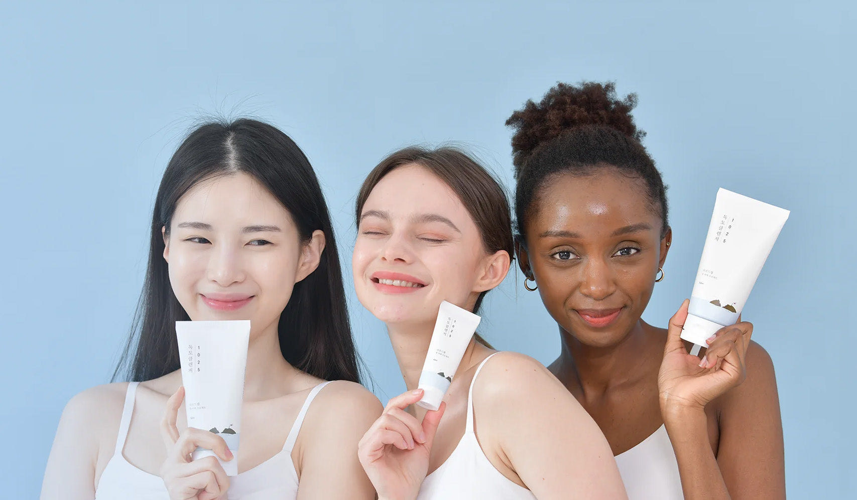 Three women holding skincare products smiling against a blue background.