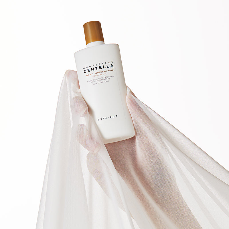 SKIN1004 Madagascar Centella Air-fit Sunscreen Plus 50ml bottle held against a sheer fabric background.