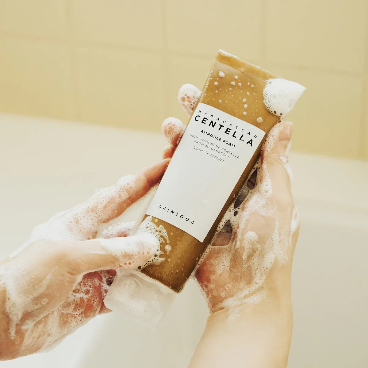 Hands holding SKIN1004 Madagascar Centella Ampoule Foam 125ml with foamy lather, showcasing the skincare product in use.