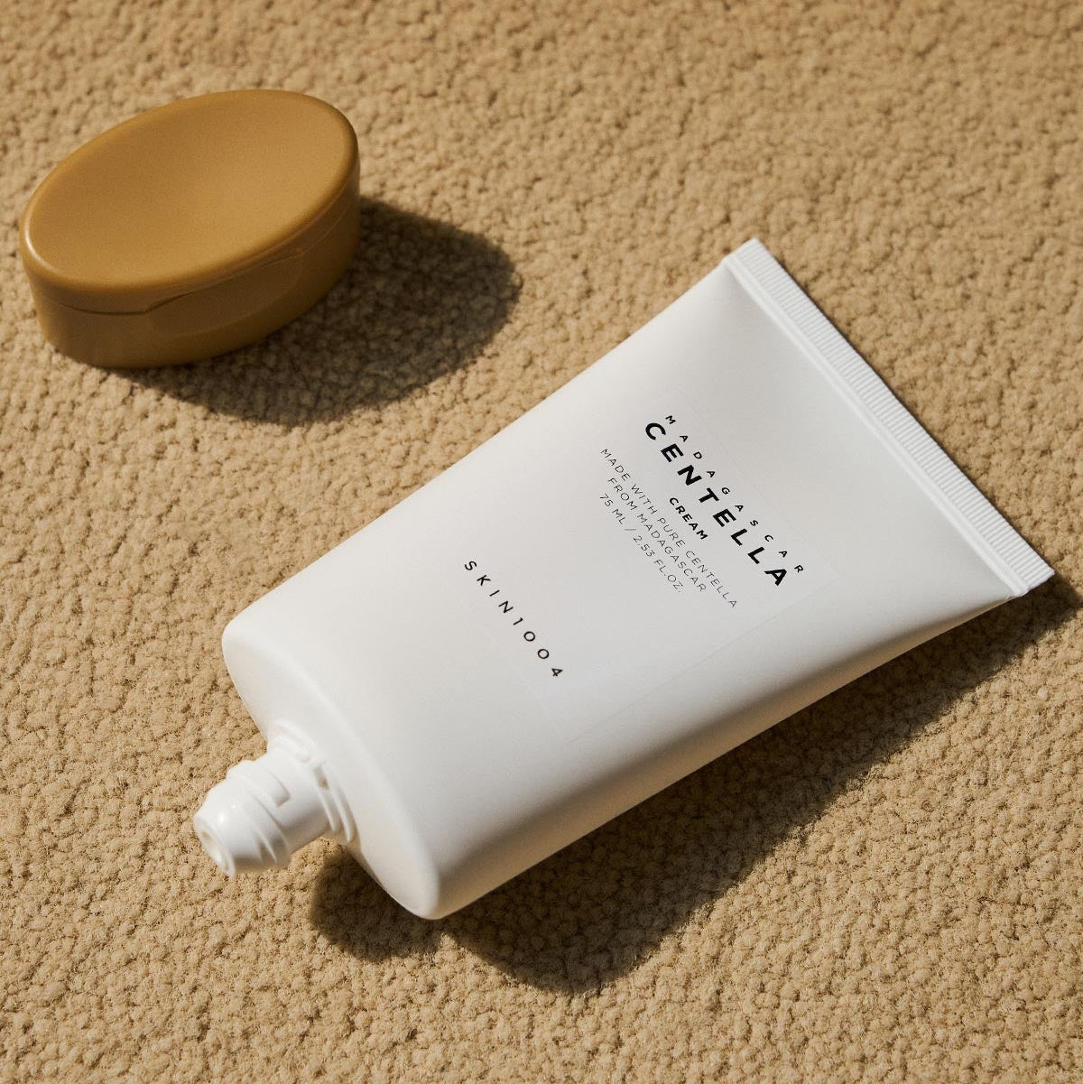 SKIN1004 Madagascar Centella Cream 75ml tube on textured background with cap beside it.