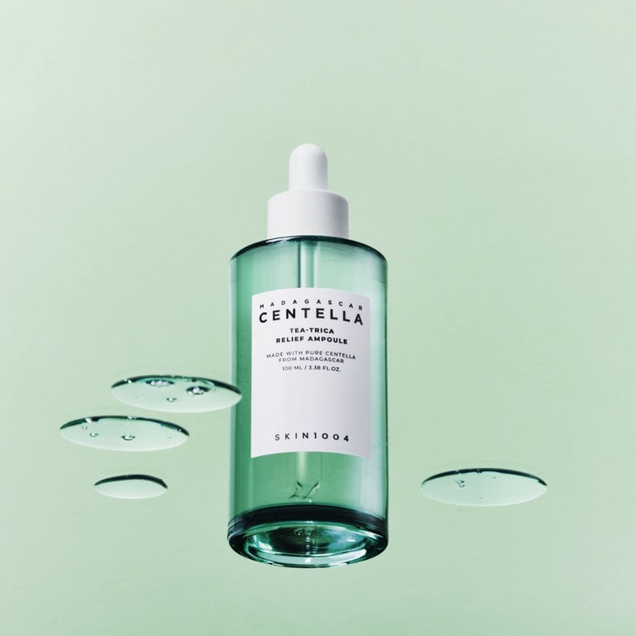 Bottle of SKIN1004 Madagascar Centella Tea-trica Relief Ampoule 100ml with droplets on a green background